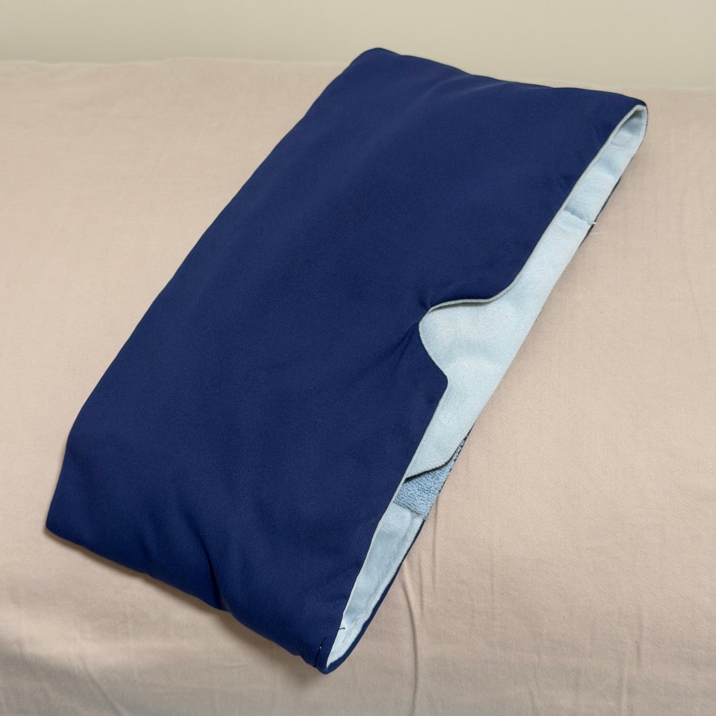 A SomniGrave Weighted Sleep Mask with navy cooling ice silk face, and a light blue soft plush lining, shown resting against a beige pillow.
